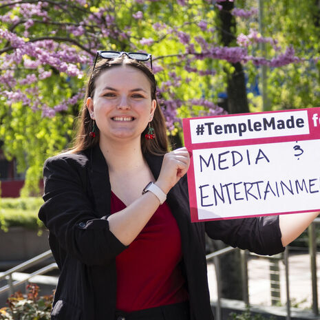 Image of Sydney Binkley holding a sign that reads "media & entertainment."