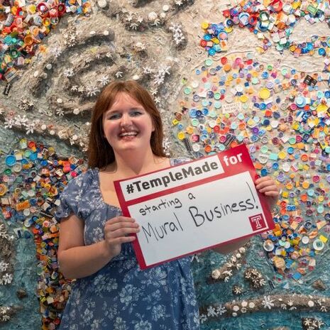 Abigail McNavage holding a #TempleMade sign in front of her painting 