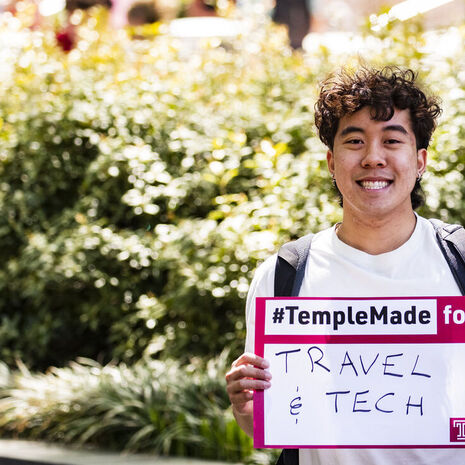 Image of Tran holding a sign that says “#TempleMade for travel and tech”