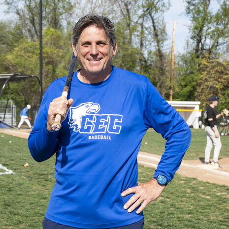 Image of a person wearing a blue shirt and holding up baseball bat on a field.     