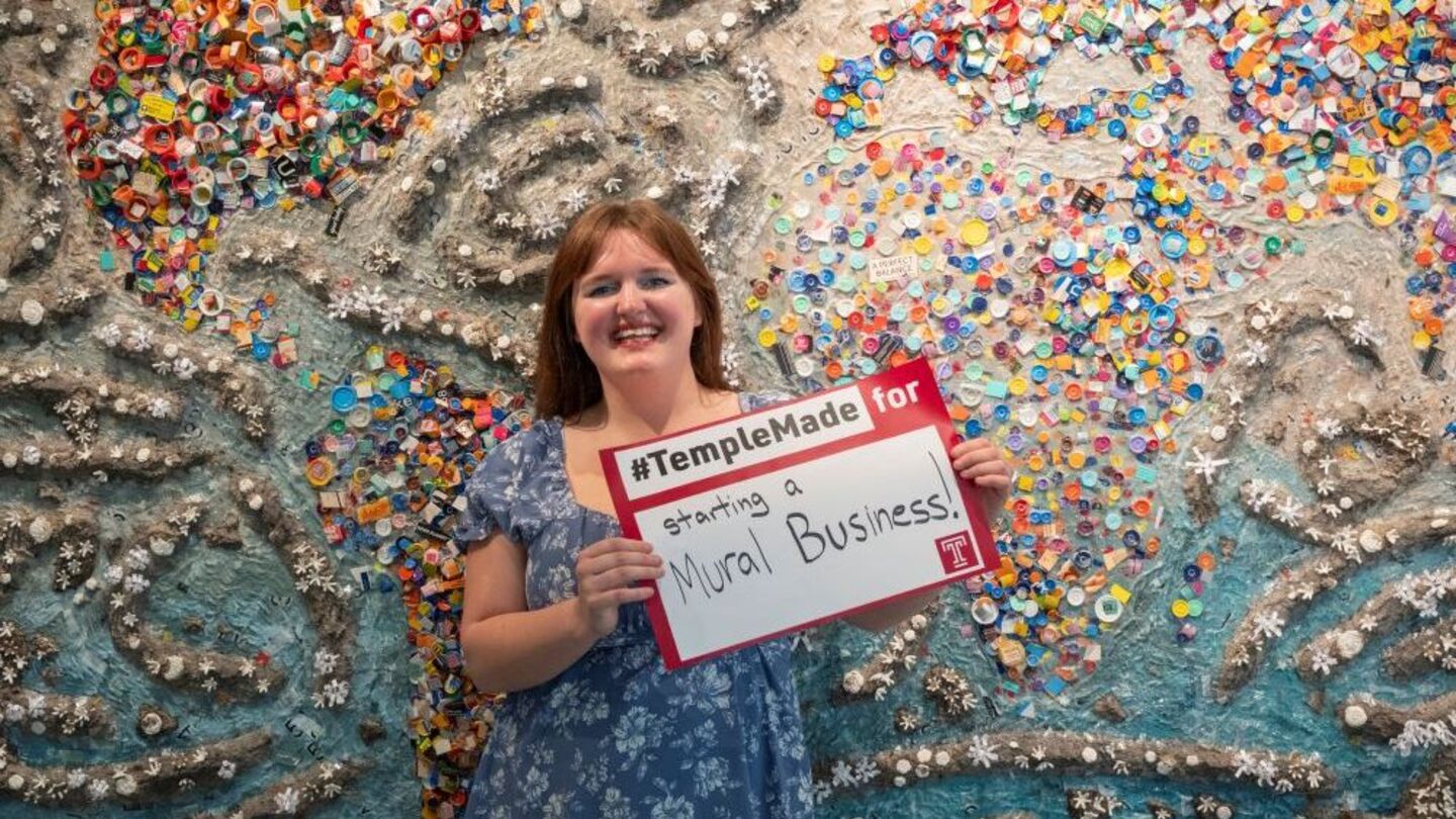 After graduation, Abigail McNavage will create her own mural business. Abigail McNavage holding a #TempleMade sign in front of her painting