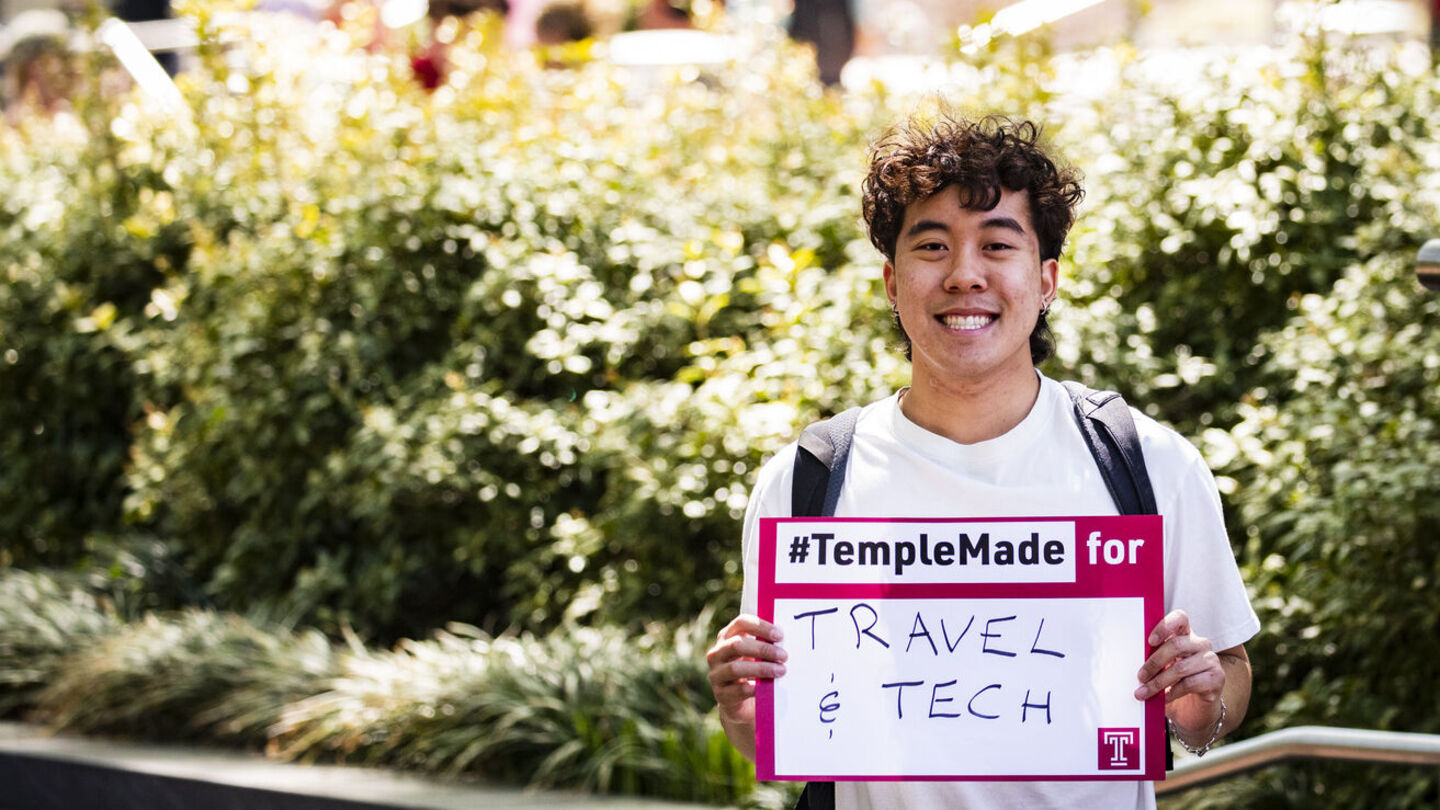 Image of Tran holding a sign that says “#TempleMade for travel and tech”